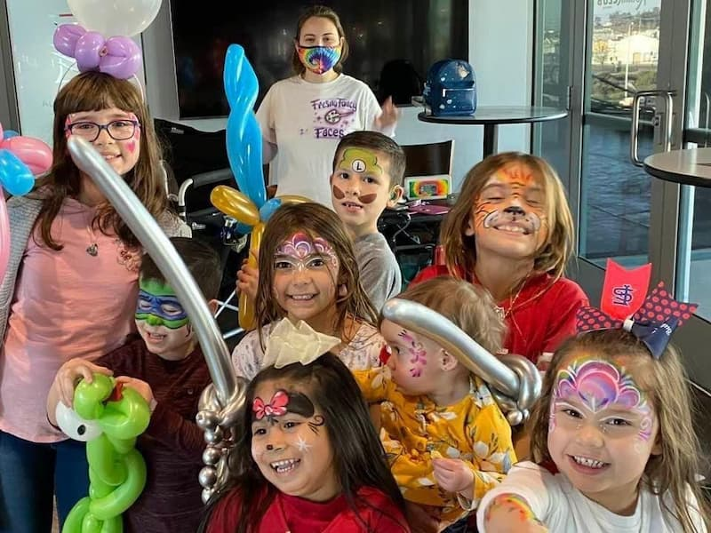 A cheerful group of children showing colorful face-painting designs at a Fresno Fancy Faces event.